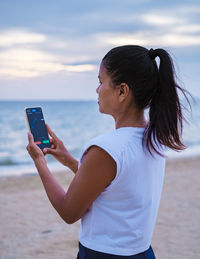 Side view of young man using mobile phone at beach