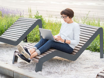 Woman sits with laptop on urban park bench. freelancer at work. student learns remotely.