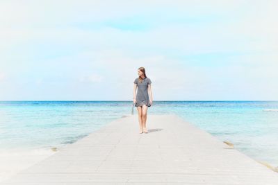Girl walking on pier over sea against sky