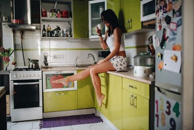 Side view of woman drinking coffee while sitting at kitchen 