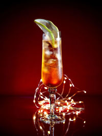 Close-up of cocktail glass with string lights against red background