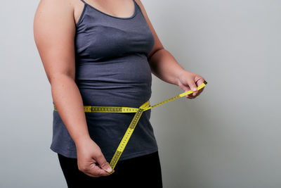 Midsection of woman measuring waist against gray background