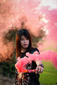 Beautiful young woman with pink flower standing against red wall