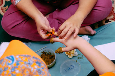 Midsection of woman applying henna tattoo on person hand