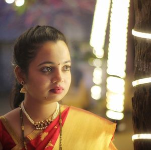 Close-up of woman in sari looking away while standing against illuminated lights