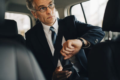 Businessman wearing wristwatch during business trip while sitting in taxi