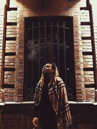 Portrait of young woman standing against window in building