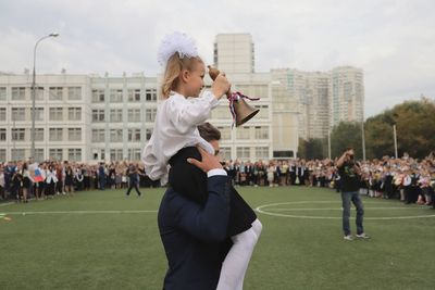 Side view of young man carrying girl on shoulders while standing on sports field