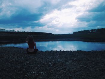 People sitting on lakeshore against cloudy sky