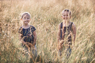Portrait of smiling siblings standing amidst plants on field