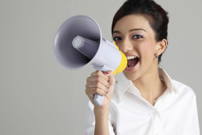 Woman screaming on megaphone while standing against white background