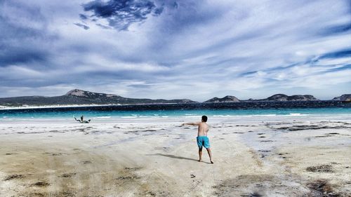 Rear view of woman walking on beach against sky