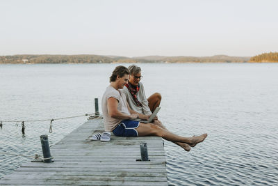 Mother with adult son on jetty looking at laptop