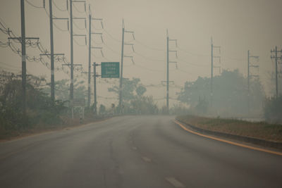 Road by electricity pylon against sky