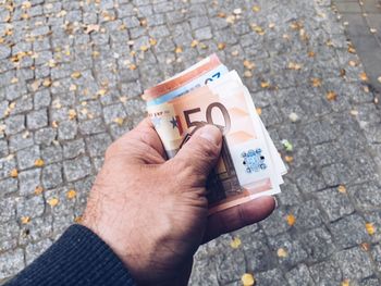 Cropped hand holding paper currency over street