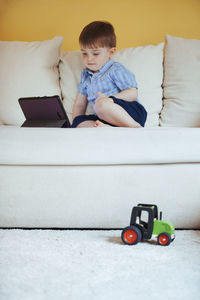 Boy looking at camera while sitting on sofa at home