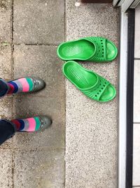 Low section of woman standing by green flip-flop on sidewalk