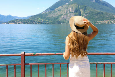 Rear view of woman standing by lake against sky