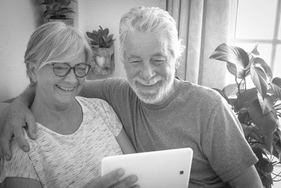 Smiling senior couple with digital tablet sitting at home
