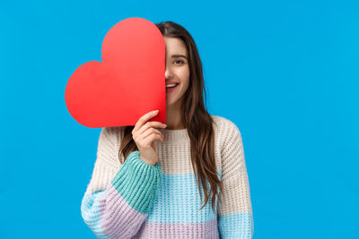 Midsection of woman holding heart shape against blue background