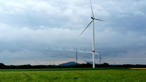 Low angle view of windmills on field against sky