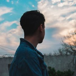 Side view of thoughtful young man looking away against sky during sunset