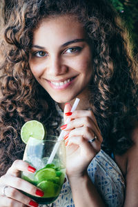 Close-up portrait of smiling young woman holding drinking glass