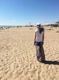 Rear view of woman standing at beach against blue sky