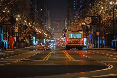 Trams on street amidst street lights and buildings during night