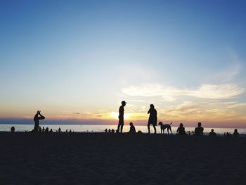 Silhouette people on beach against sky during sunset