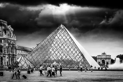 Group of people in front of building against cloudy sky