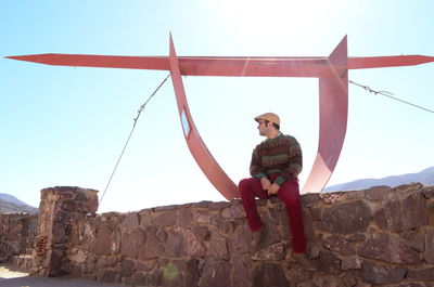 Full length of man sitting on rock against sky