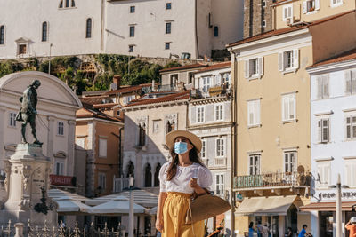Female tourist wearing face mask, walking in square of idyllic town of piran, slovenia