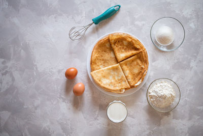 Top view of raw brown eggs, flour, milk, sugar and whisk as ingredients of batter or dough pancakes