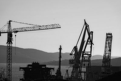 Silhouette cranes at construction site against clear sky