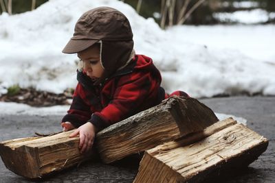 Close-up of boy holding firewood on road during winter
