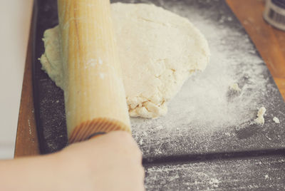 Cropped hand of woman pressing dough with rolling pin