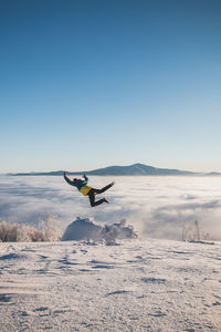 Energetic boy in winter clothes jumping from a stump into the fresh snow with a view of the sunrise