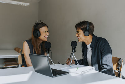 Happy male and female students looking at each other during podcasting in classroom