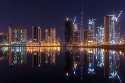 Illuminated cityscape reflecting in sea against sky at night
