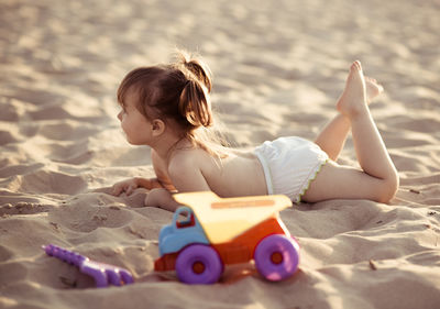 Cute girl lying by toy truck on sand at beach