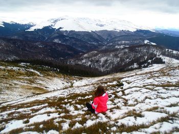 Rear view of child on snowcapped mountain against sky