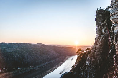 Scenic view of river by mountains against clear sky during sunset