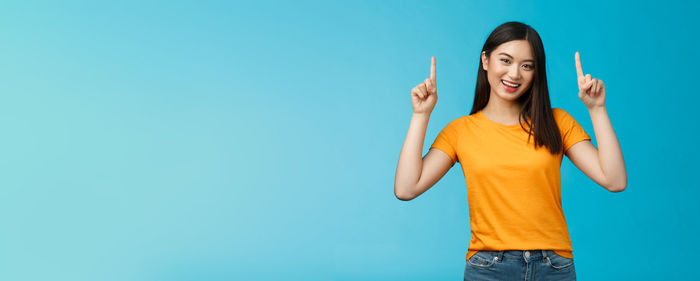 Young woman with arms raised standing against blue background