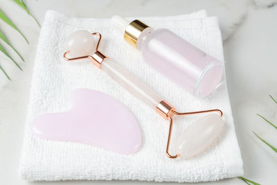 Pink quartz gua sha scraper and roller face massager and bottle of cosmetic serum for the face 