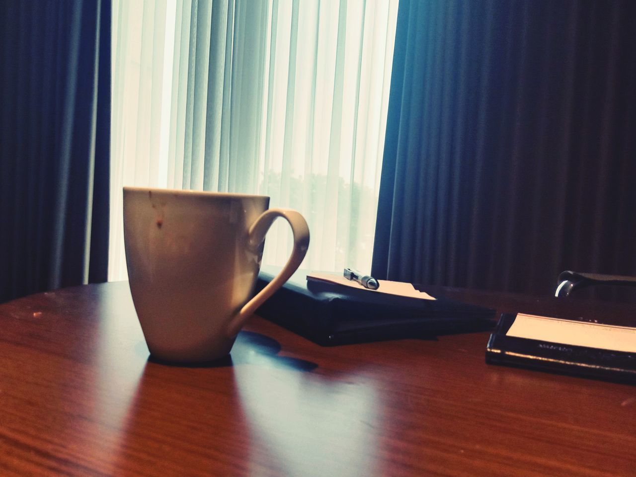 table, indoors, curtain, interior design, window covering, cup, no people, mug, tableware, wood, coffee cup, room, home interior, furniture, blue, window, desk, still life, business, office, technology, communication, laptop, window treatment, drink