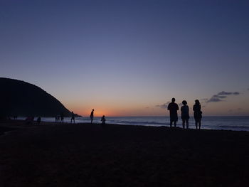 Silhouette people at beach against sky during sunset