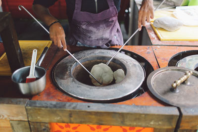 Midsection of vendor baking naan breads in oven at stall