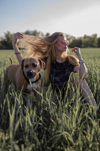 Young woman with dog sitting on grassy field against clear sky