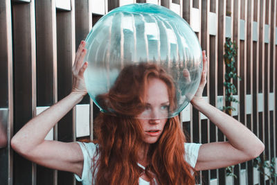 Close-up of young woman removing glass helmet from head against metallic railing